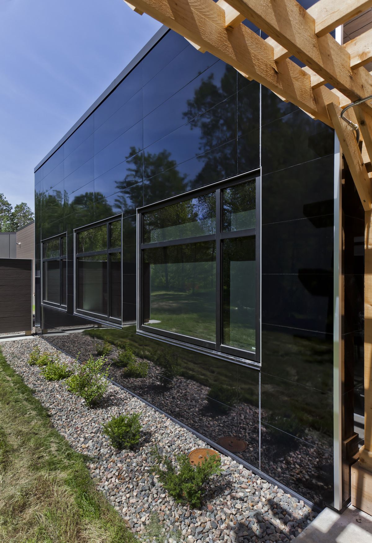 Side of Paul Bunyan building with Miraia panels in Onyx showing reflection of trees