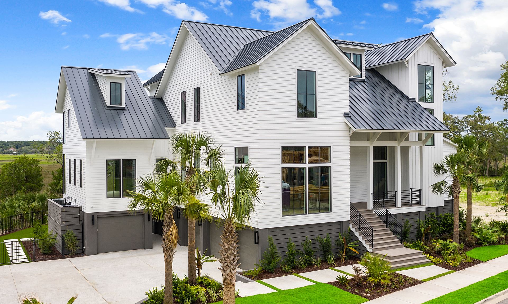 A side look at a home with NichiPanel primed siding painted white and a black roof, along with black framed windows, surrounded by palm trees and green grass. 